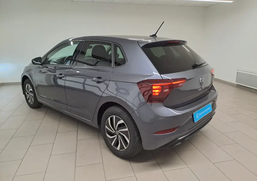 Volkswagen Polo gris cendre vue 3/4 arrière droit en intérieur, feux arrière allumés et jantes spécifiques VW Edition.