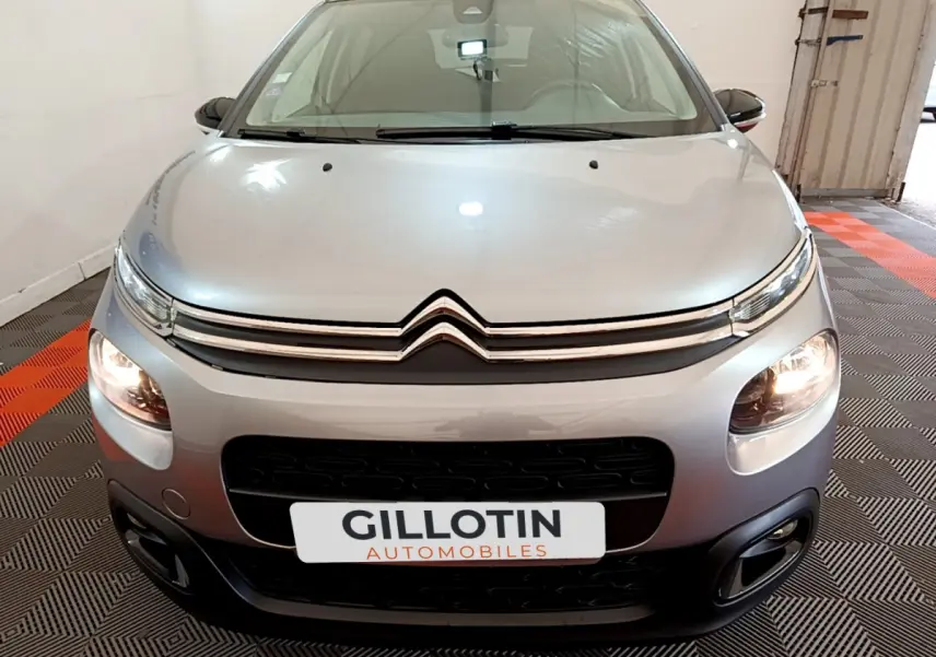 Vue frontale d'une Citroën C3 gris clair 2019 avec phares allumés et calandre distinctive en double chevron.