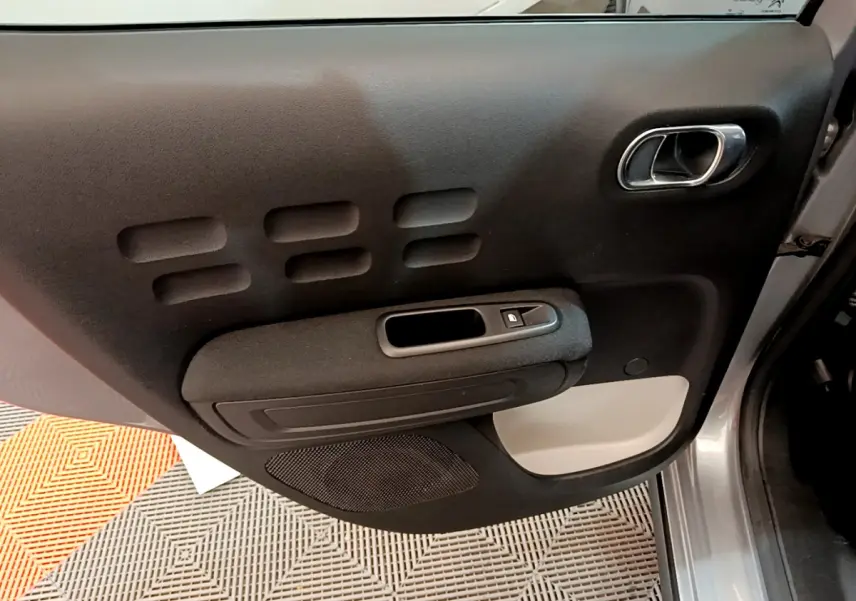Gros plan sur la porte intérieure côté droit gris clair de la Citroën C3 avec poignée chromée et commande de fenêtre.