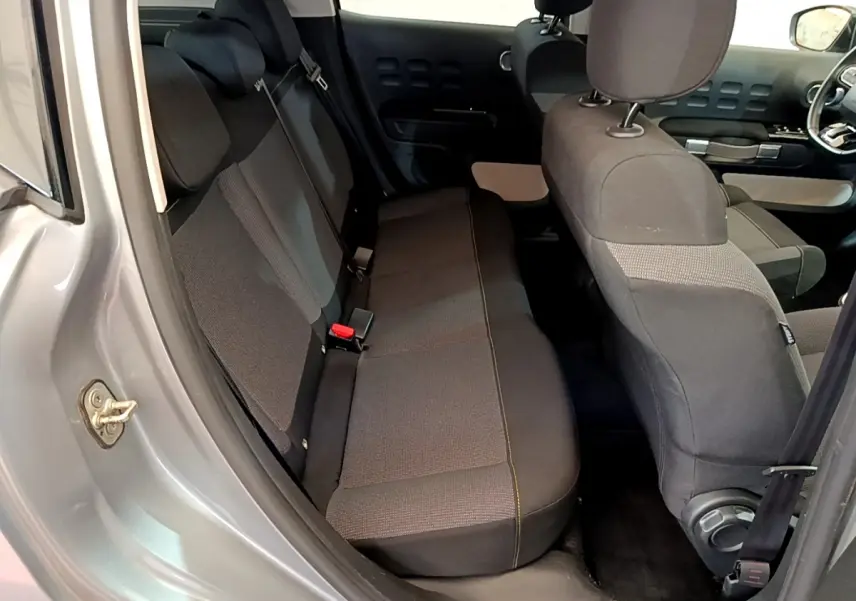 Vue intérieure côté arrière droit de la Citroën C3 gris clair, montrant la banquette arrière et les sièges avant en tissu noir.