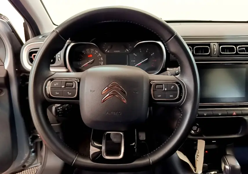 Vue intérieure centrée sur le volant cuir de la Citroën C3 gris clair avec tableau de bord et écran tactile.