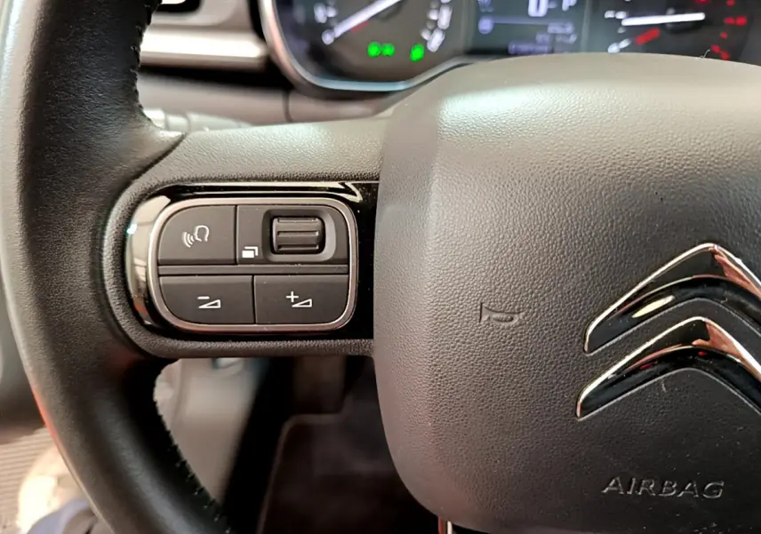 Gros plan sur le volant cuir noir de la Citroën C3 gris clair, avec commandes vocales et volume intégrées à gauche.