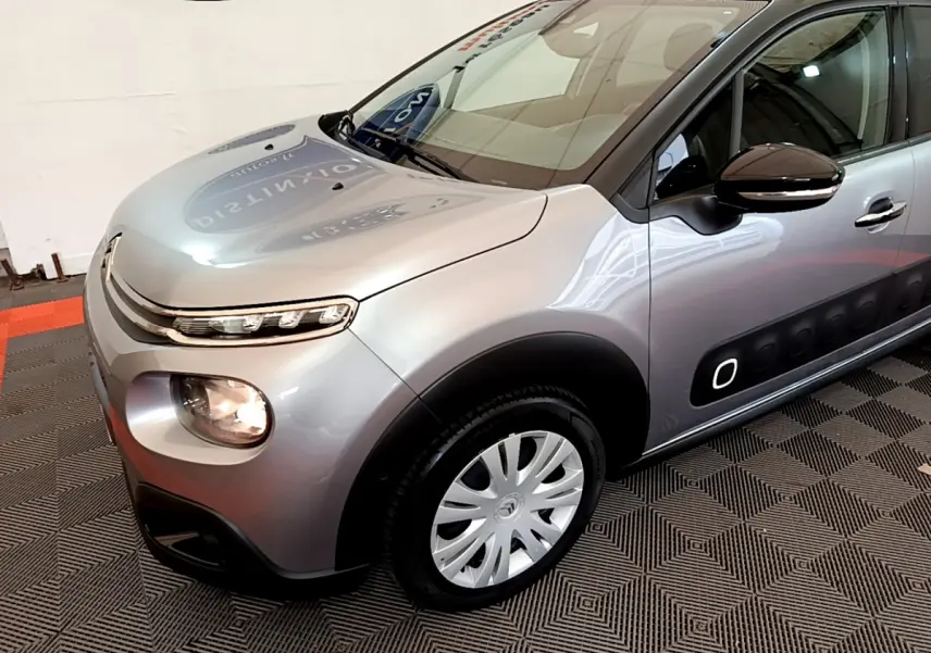 Vue 3/4 avant droit d'une Citroën C3 gris clair avec protections latérales noires et jantes argentées.