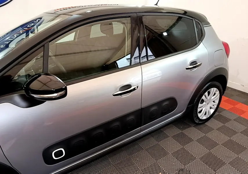Profil côté gauche d'une Citroën C3 gris clair avec protections noires caractéristiques et rétroviseur noir brillant.