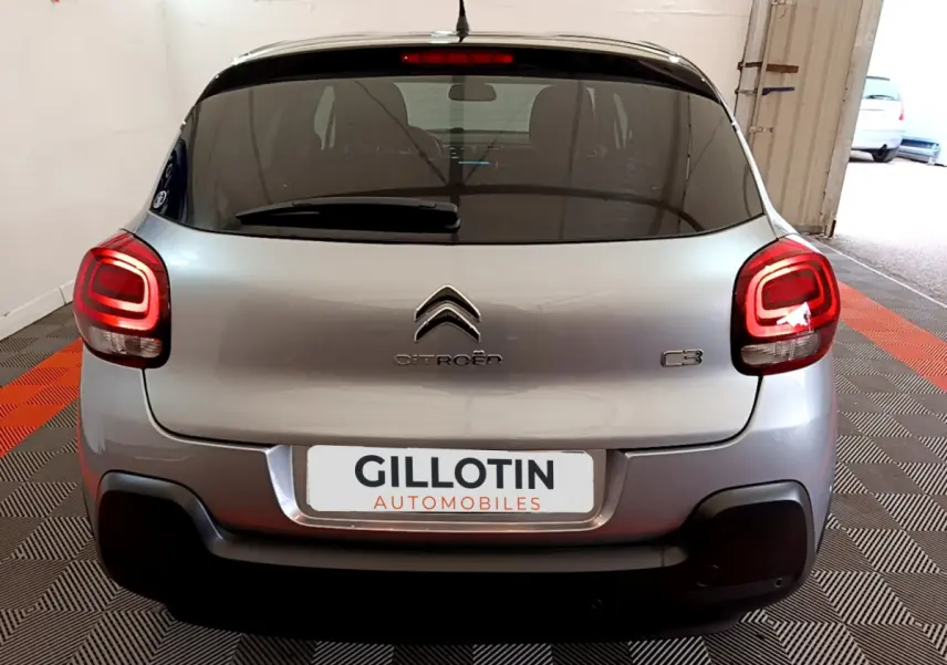 Vue arrière d'une Citroën C3 gris clair avec feux arrière allumés dans un garage fermé.
