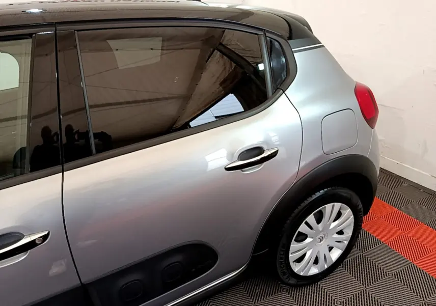 Vue latérale arrière droite d'une Citroën C3 gris clair avec poignées chromées et protections noires sur porte.