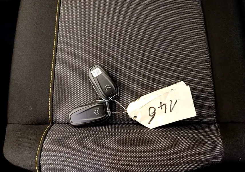 Clé de voiture Citroën posée sur un siège tissu gris foncé avec surpiqûres jaunes, vue de dessus.