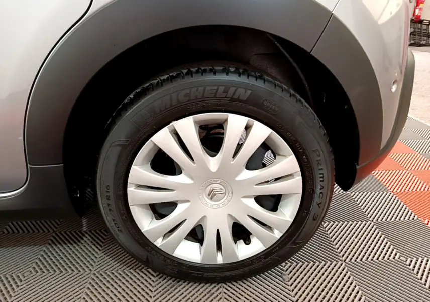 Gros plan sur la roue avant droite d'une Citroën C3 gris clair, avec jante acier et enjoliveur blanc éclatant.