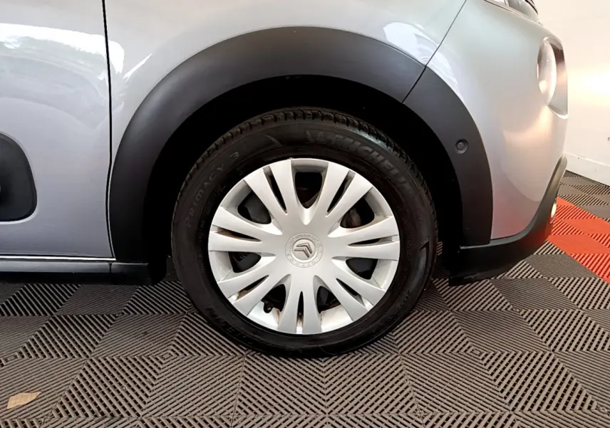 Gros plan sur la roue avant droite d'une Citroën C3 gris clair avec jante acier et enjoliveur blanc.