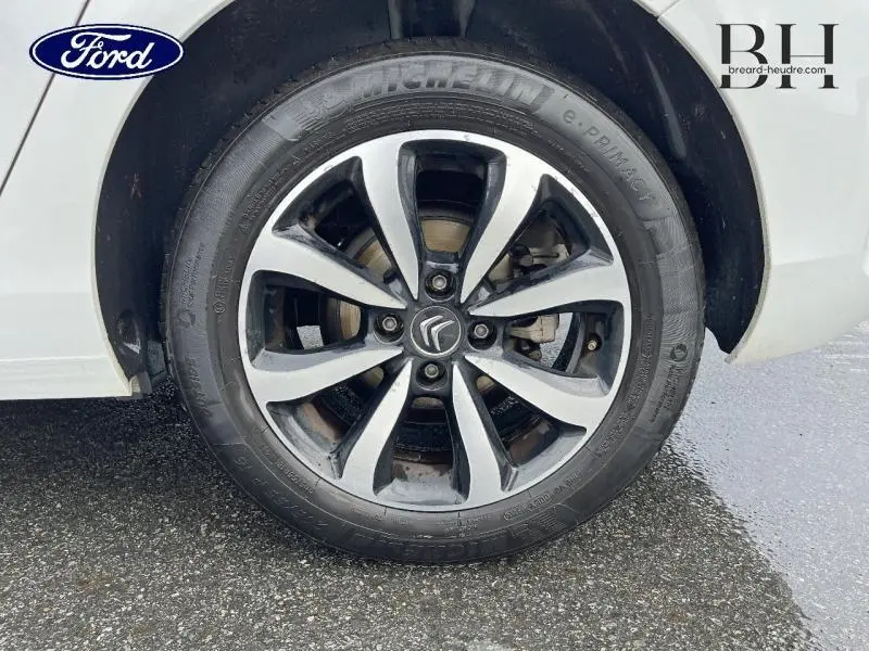 Gros plan sur la roue avant gauche d'une Citroën C4 blanche avec jante alliage bicolore et logo Citroën central.