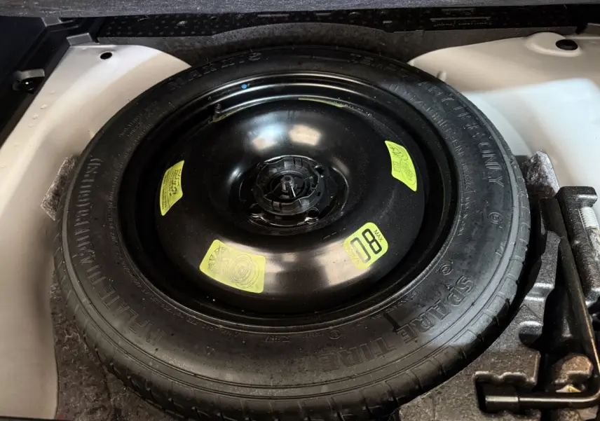 Vue rapprochée de la roue de secours noire dans le coffre blanc d’un Peugeot 2008 BlueHDi 130 de 2021.