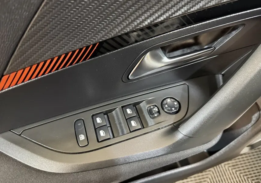 Gros plan sur la commande des vitres et rétroviseurs côté conducteur d’un Peugeot 2008 blanc, intérieur noir avec insert orange.