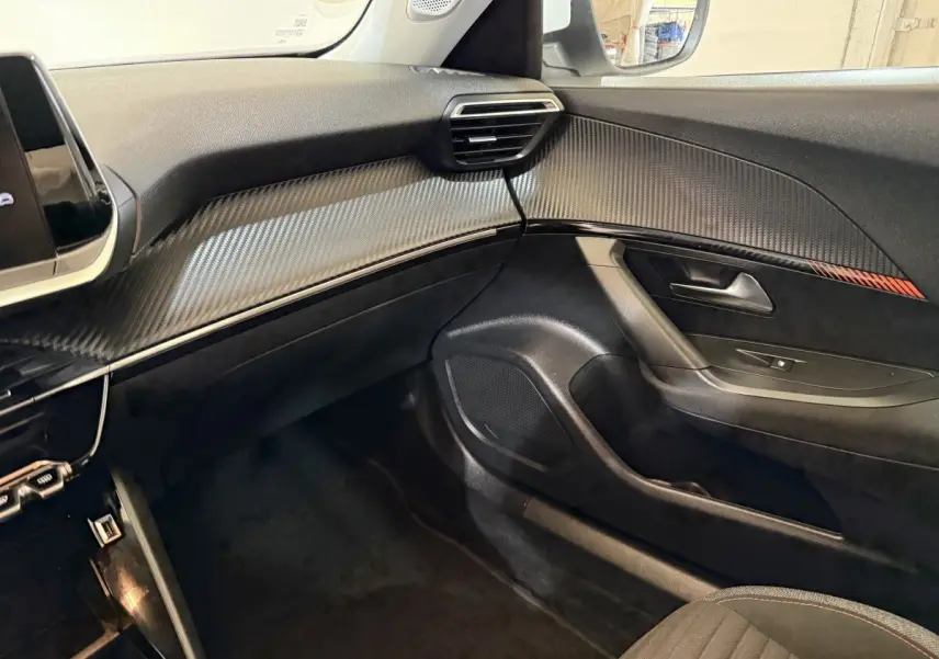 Vue intérieure côté passager du Peugeot 2008 2021, tableau de bord noir avec insert effet carbone et détails rouges.