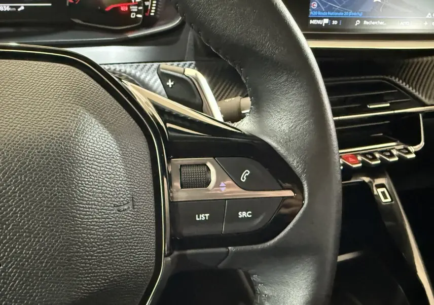 Gros plan sur le volant cuir noir du Peugeot 2008 2021, avec commandes audio et écran tactile du tableau de bord visible.