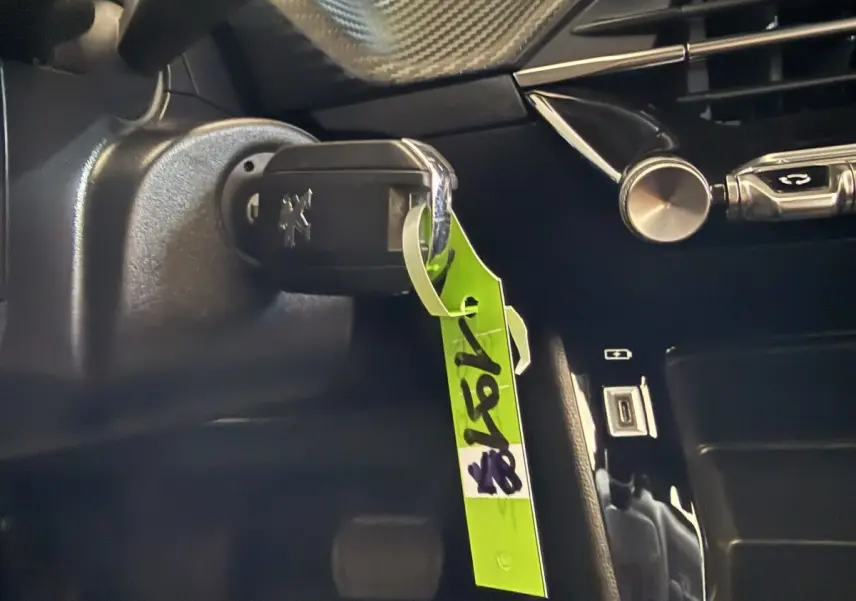 Gros plan intérieur sur la clé de contact Peugeot 2008 avec porte-clés vert, tableau de bord noir en arrière-plan.