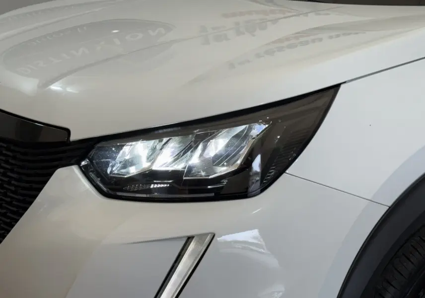 Gros plan sur le phare avant droit LED du Peugeot 2008 blanc, soulignant la calandre et l'aile avant.