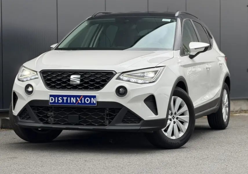 Vue 3/4 avant d’un SEAT Arona blanc avec toit noir, calandre noire et jantes alliage 16 pouces, sur fond urbain.