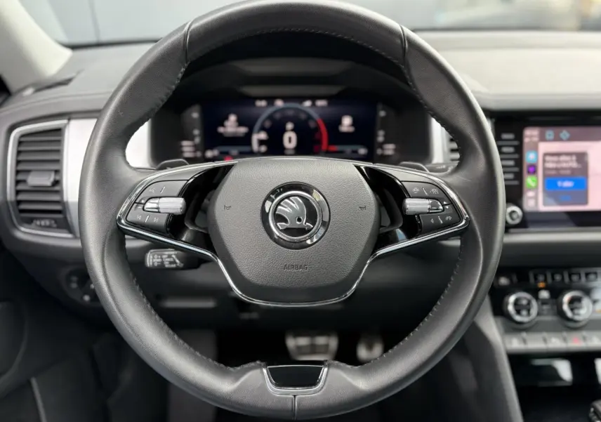 Volant cuir noir avec logo Skoda au centre, tableau de bord numérique et écran tactile du Skoda Kodiaq 2024 visible en arrière-plan.