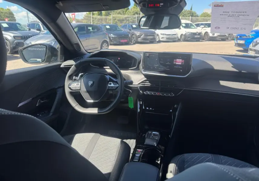 Vue intérieure avant du Peugeot 2008 Hybrid noir, montrant le volant compact, l'écran tactile central et les sièges tissu.