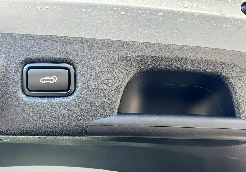 Bouton d'ouverture électrique du coffre sur panneau intérieur noir d'une KIA Xceed gris 3/4 arrière.