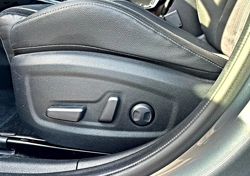 Gros plan sur les commandes électriques du siège conducteur en cuir noir du KIA Xceed gris 2024, côté gauche.