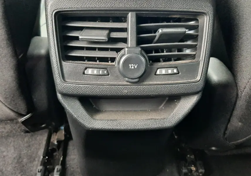 Gros plan sur la sortie d'air arrière noire avec prise 12V du Peugeot 3008 Hybrid 2024, intérieur gris foncé.