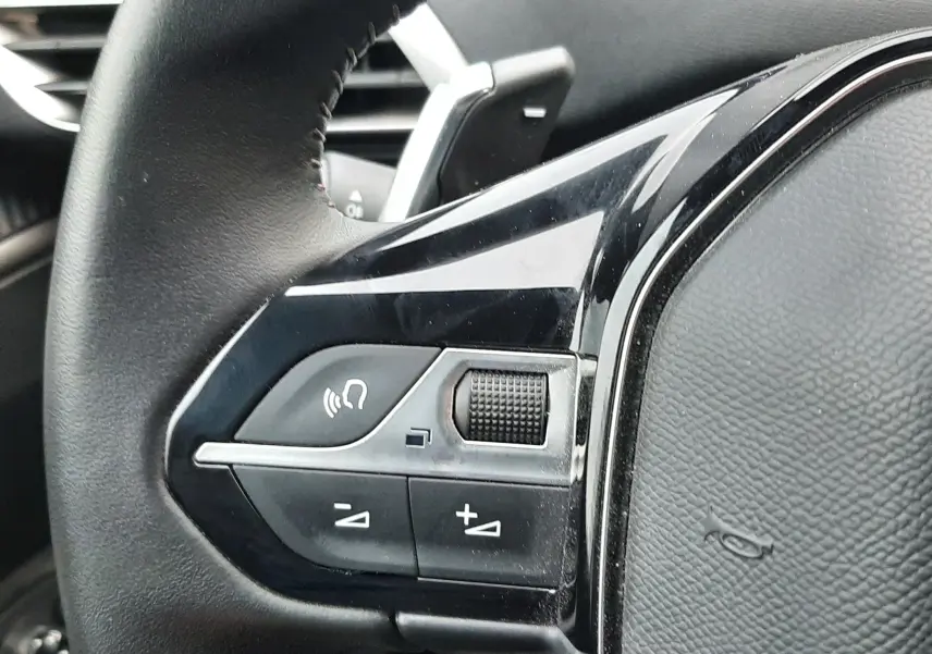 Gros plan sur les commandes gauche du volant cuir noir du Peugeot 3008 Hybrid 2024, avec molette et boutons de réglage.