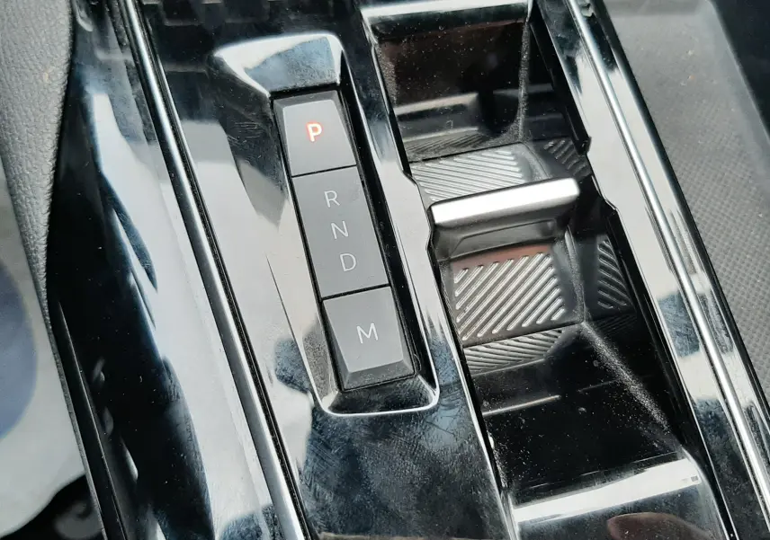 Gros plan sur la console centrale noire brillante du Peugeot 3008 Hybrid 136 e-DCS6 Allure Pack avec sélecteur de boîte auto.