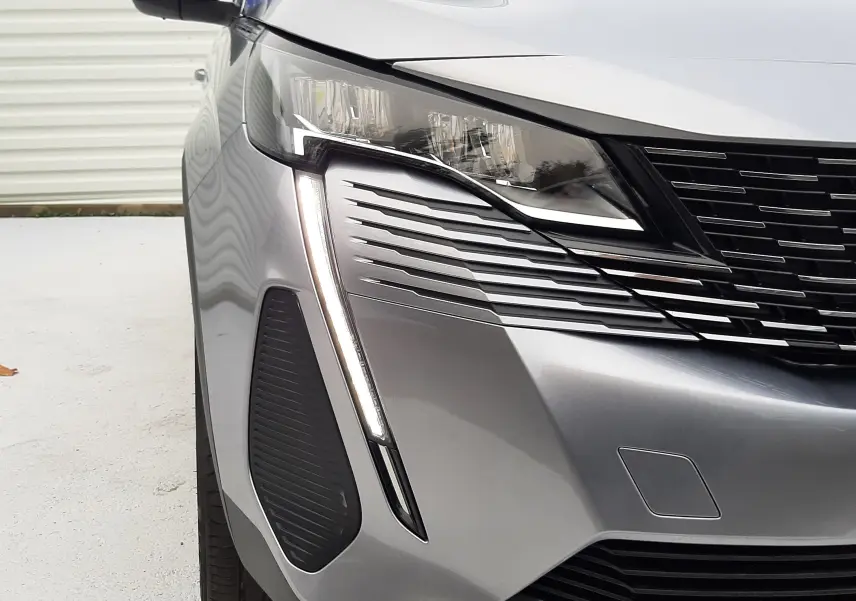 Gros plan sur l'avant gauche du Peugeot 3008 Hybrid gris Artense, mettant en valeur son phare LED et la calandre noire.