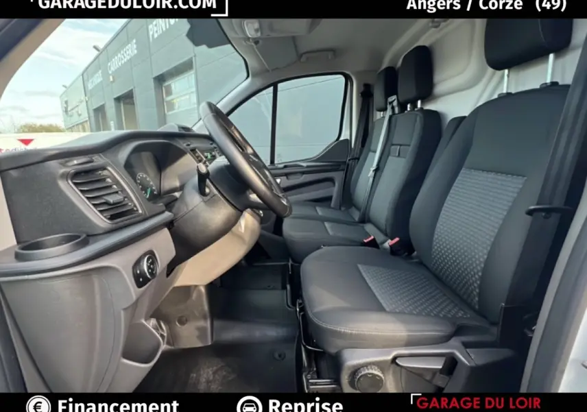 Vue intérieure côté conducteur du Ford Transit Custom blanc, montrant les sièges avant et le volant multifonctions cuir et alu.