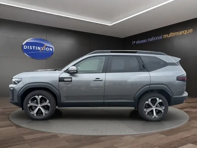 Vue latérale droite du Dacia Bigster gris foncé avec jantes alliage et barres de toit noires en showroom.