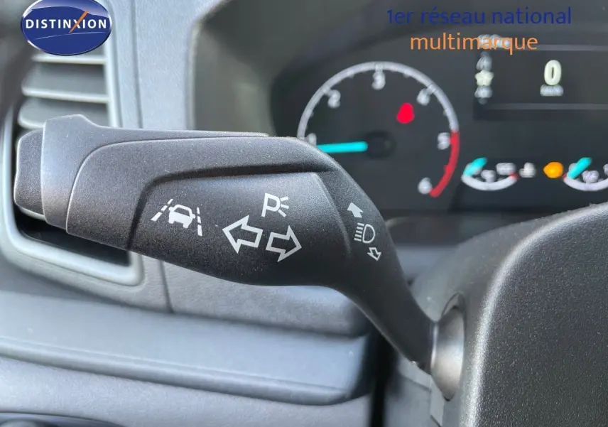 Gros plan sur la commande de clignotant du Ford Transit Fourgon blanc, avec tableau de bord en arrière-plan flou.