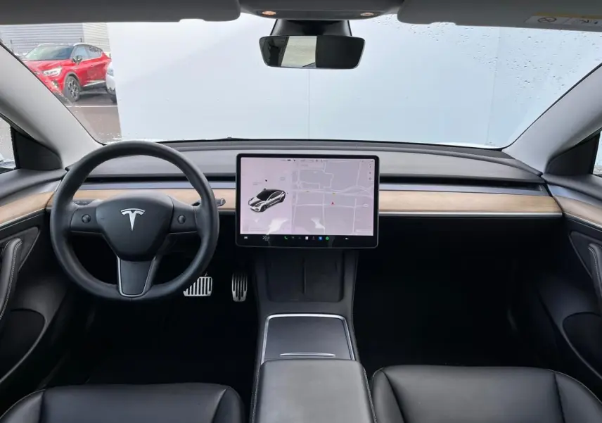 Intérieur noir et bois clair d'une Tesla Model 3 2022, vue frontale sur le tableau de bord et écran tactile central.