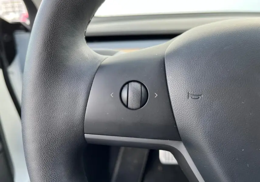 Gros plan sur la molette de commande gauche du volant noir d'une Tesla Model 3 Standard Plus RWD blanche de 2022.