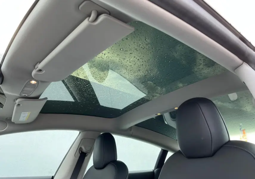 Toit panoramique en verre avec gouttes d'eau et sièges avant noirs de la Tesla Model 3 blanche vue de l'intérieur