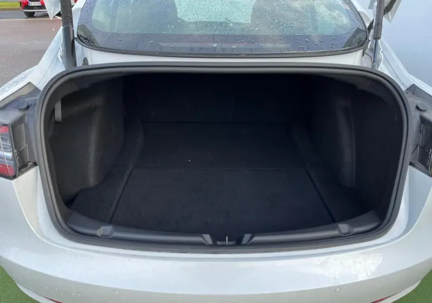 Coffre ouvert vu de l'arrière d'une Tesla Model 3 blanche 2022, intérieur spacieux et noir.