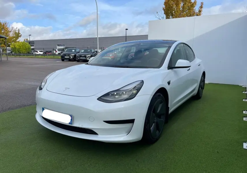 Tesla Model 3 blanc vue 3/4 avant droit avec toit panoramique en verre et jantes noires sur parking.