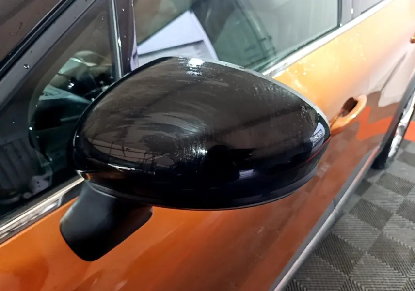 Rétroviseur noir côté gauche d’un Renault Captur jaune vu en gros plan, avec porte et poignée visibles.