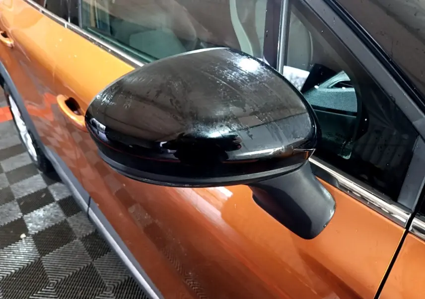 Gros plan sur le rétroviseur noir côté conducteur d’un Renault Captur jaune vu de profil gauche.