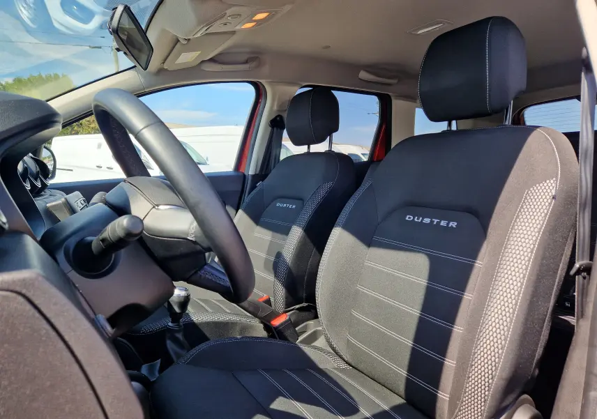 Vue intérieure côté conducteur du Dacia Duster 2021 rouge fusion, mettant en valeur les sièges noirs avec logo DUSTER brodé.