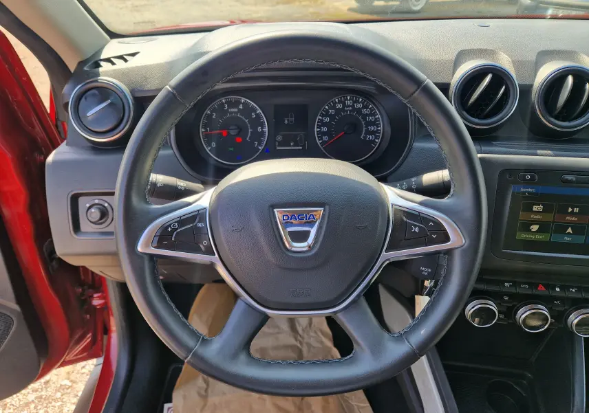 Vue intérieure centrée sur le volant du Dacia Duster rouge fusion 2021, avec tableau de bord et écran tactile visibles.