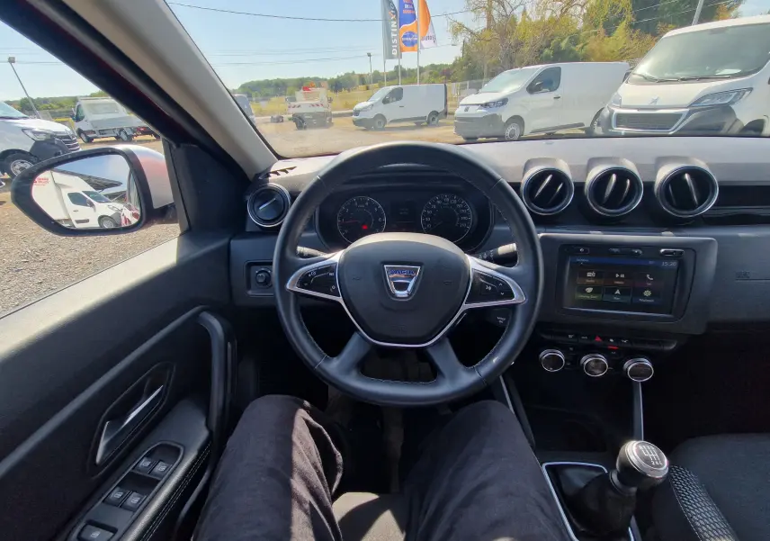 Vue intérieure centrée sur le volant et tableau de bord du Dacia Duster 2021, boîte manuelle, avec écran tactile et commandes au volant.