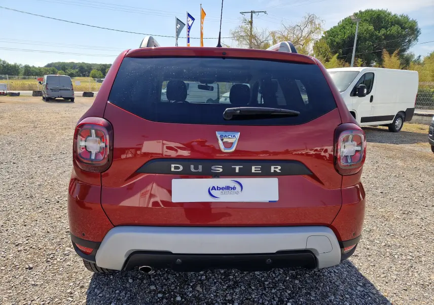 Vue arrière d'un Dacia Duster rouge fusion 2021 avec feux arrière caractéristiques et logo central visible.
