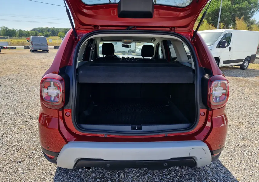 Vue arrière du Dacia Duster rouge fusion 2021 avec coffre ouvert et cache-bagages visible en extérieur.