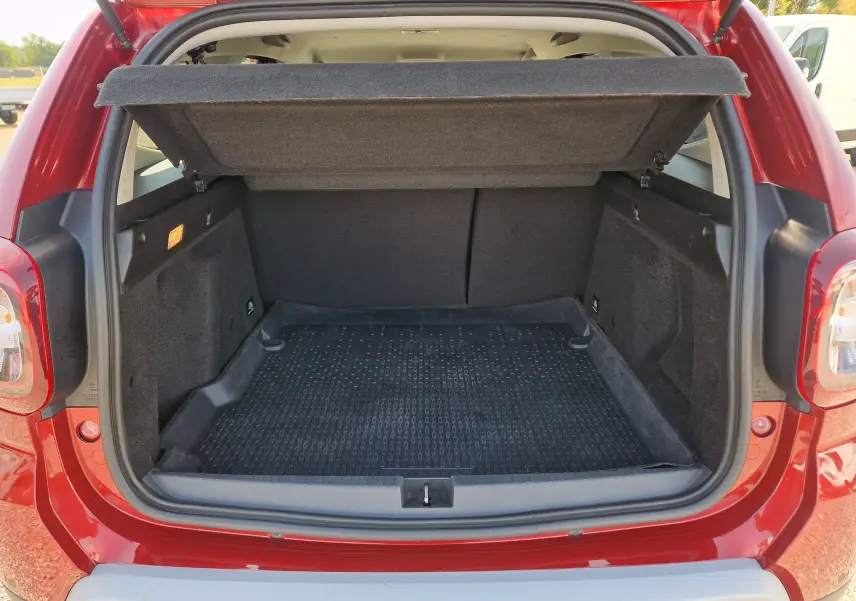 Coffre ouvert vu de l’arrière d’un Dacia Duster rouge fusion 2021, montrant un espace de chargement vide avec tapis noir.
