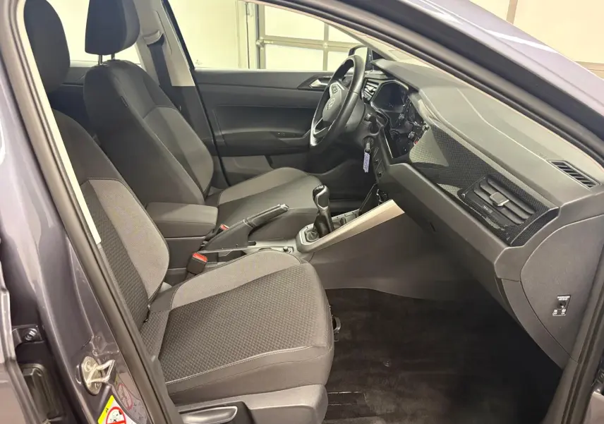 Vue intérieure côté conducteur de la Volkswagen Polo gris cendre 2024, avec sièges tissu et boîte manuelle visible.