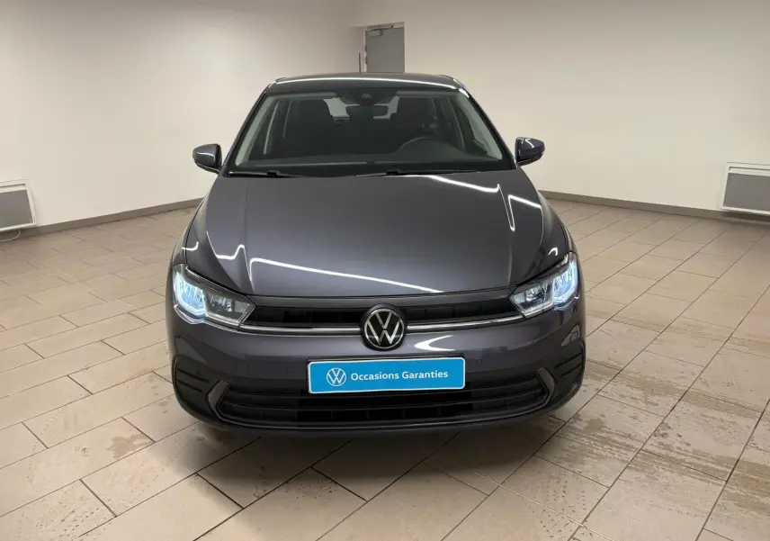 Volkswagen Polo gris cendre vue de face en intérieur, phares allumés et logo VW bien visible.
