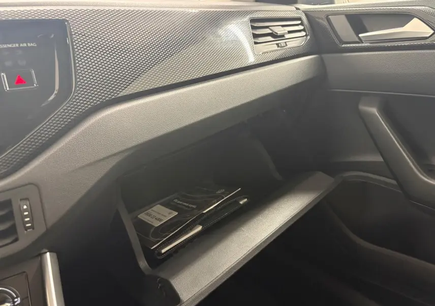 Intérieur de la Volkswagen Polo 2024 gris cendre, vue côté passager sur la boîte à gants ouverte avec documents visibles.