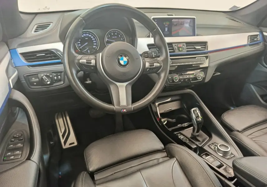 Vue intérieure avant du BMW X1 sDrive18i M Sport 2019, volant cuir, tableau de bord avec écran tactile et détails bleus.