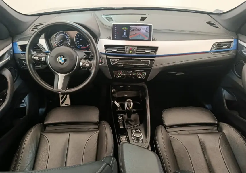 Vue intérieure avant du BMW X1 sDrive18i M Sport 2019, sièges cuir noirs et écran tactile affichant la caméra de recul.